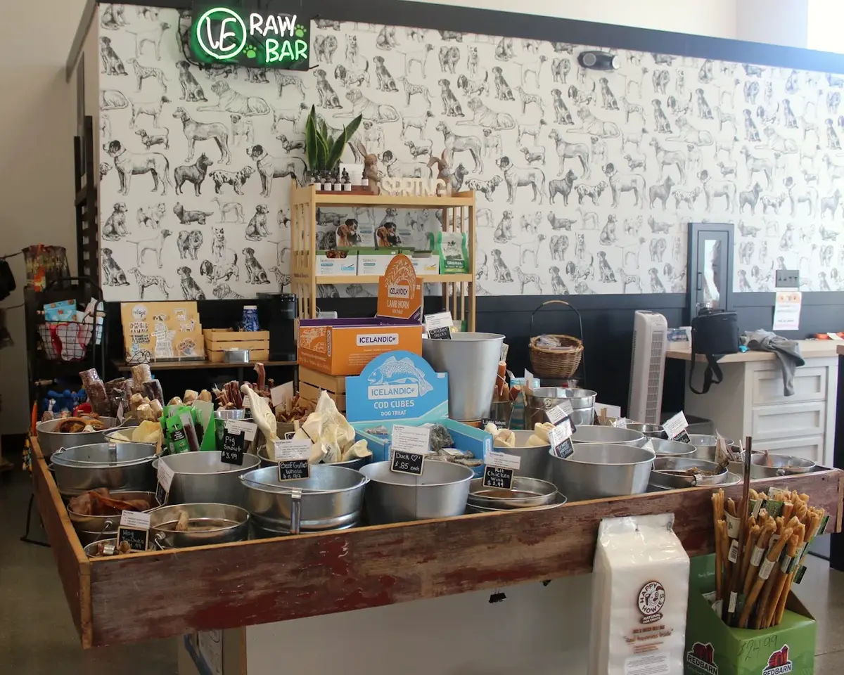 The raw bar: a rustic wood table of steel bins filled with chews, priced on chalkboard tags, under a neon Raw Bar sign